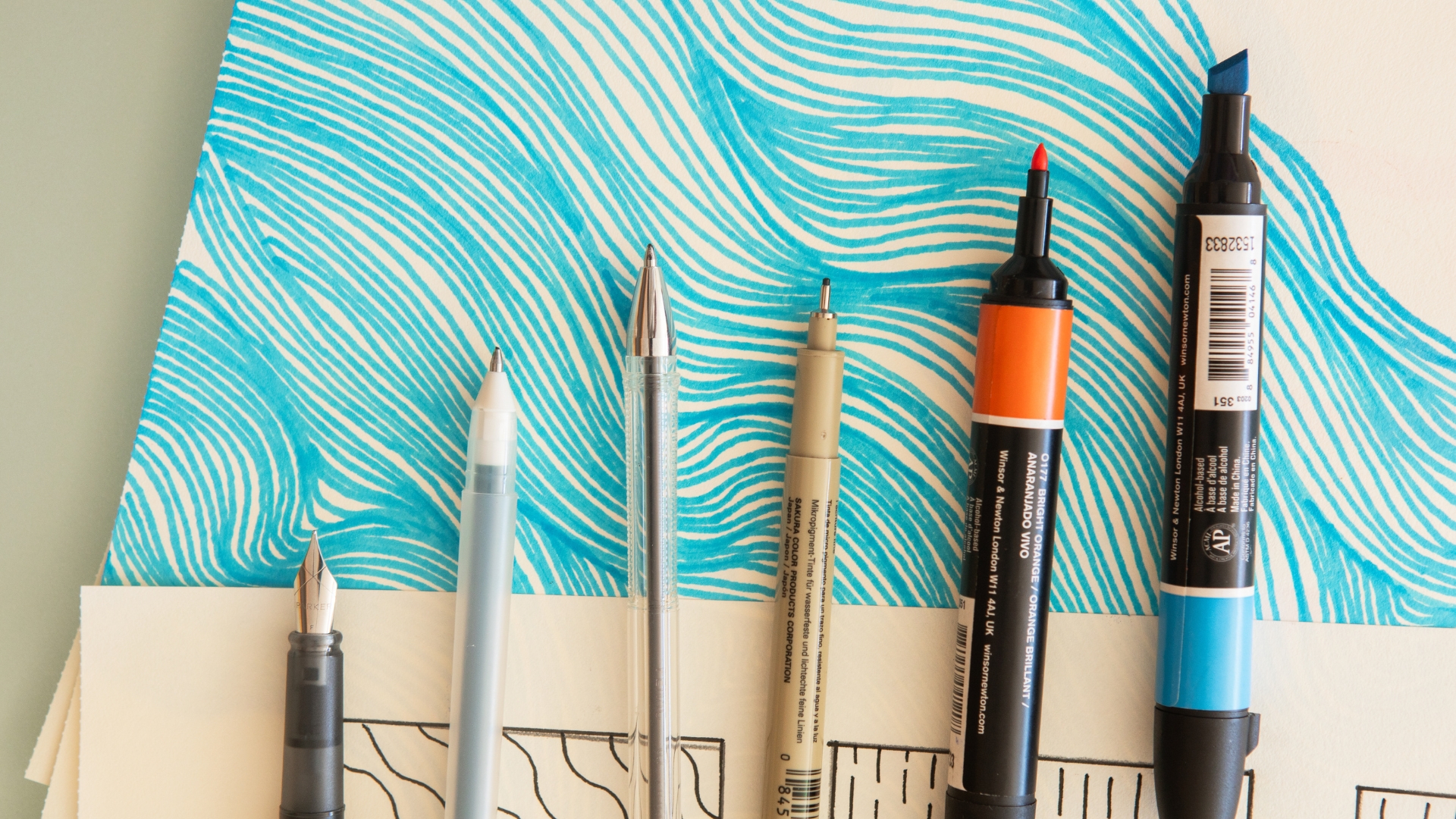 Meditative Drawing - Writing objects rest atop a drawing of blue wavy lines on white paper.
